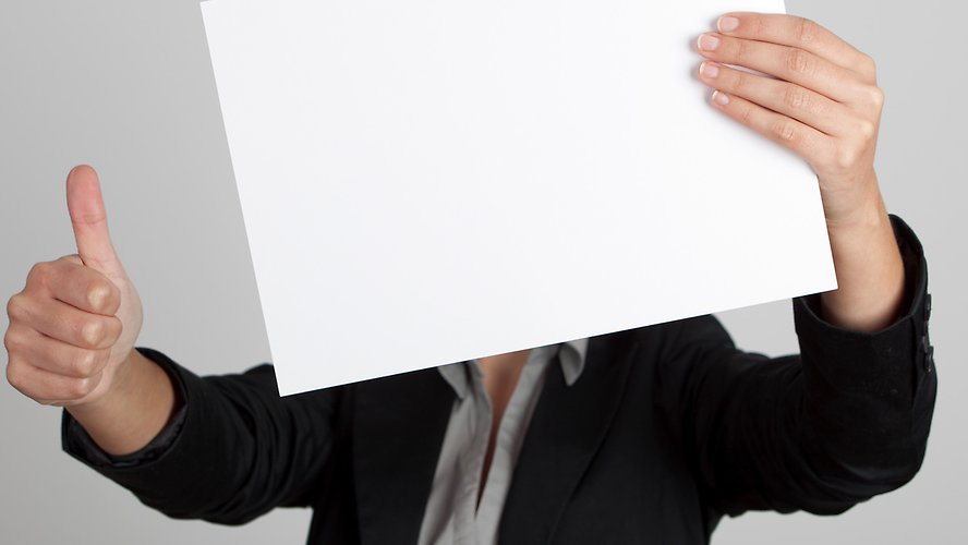 Woman showing a blank paper sheet in front of her head and making a thumbs up gesture with the right hand